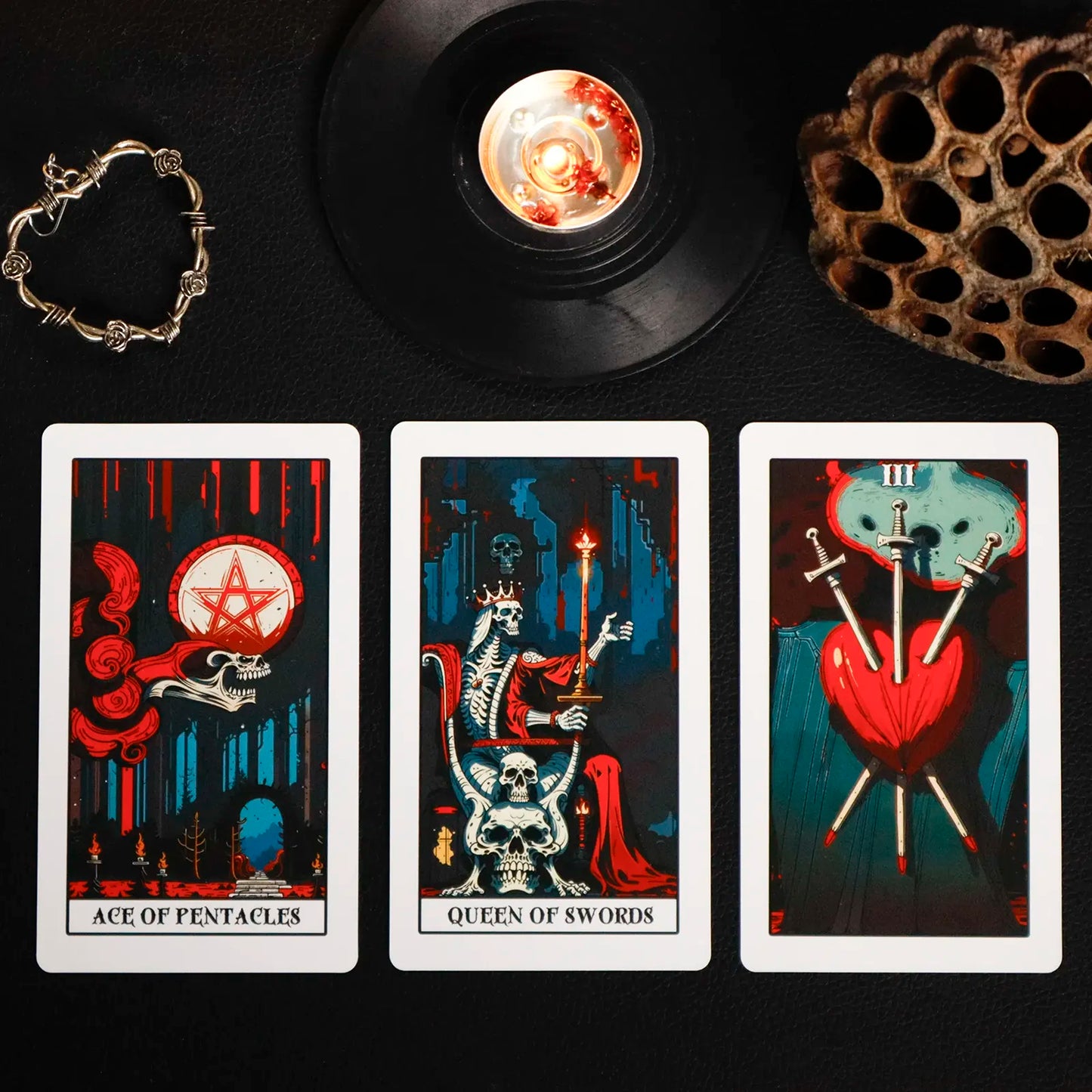 Three tarot cards with a candle and bracelet on a dark surface