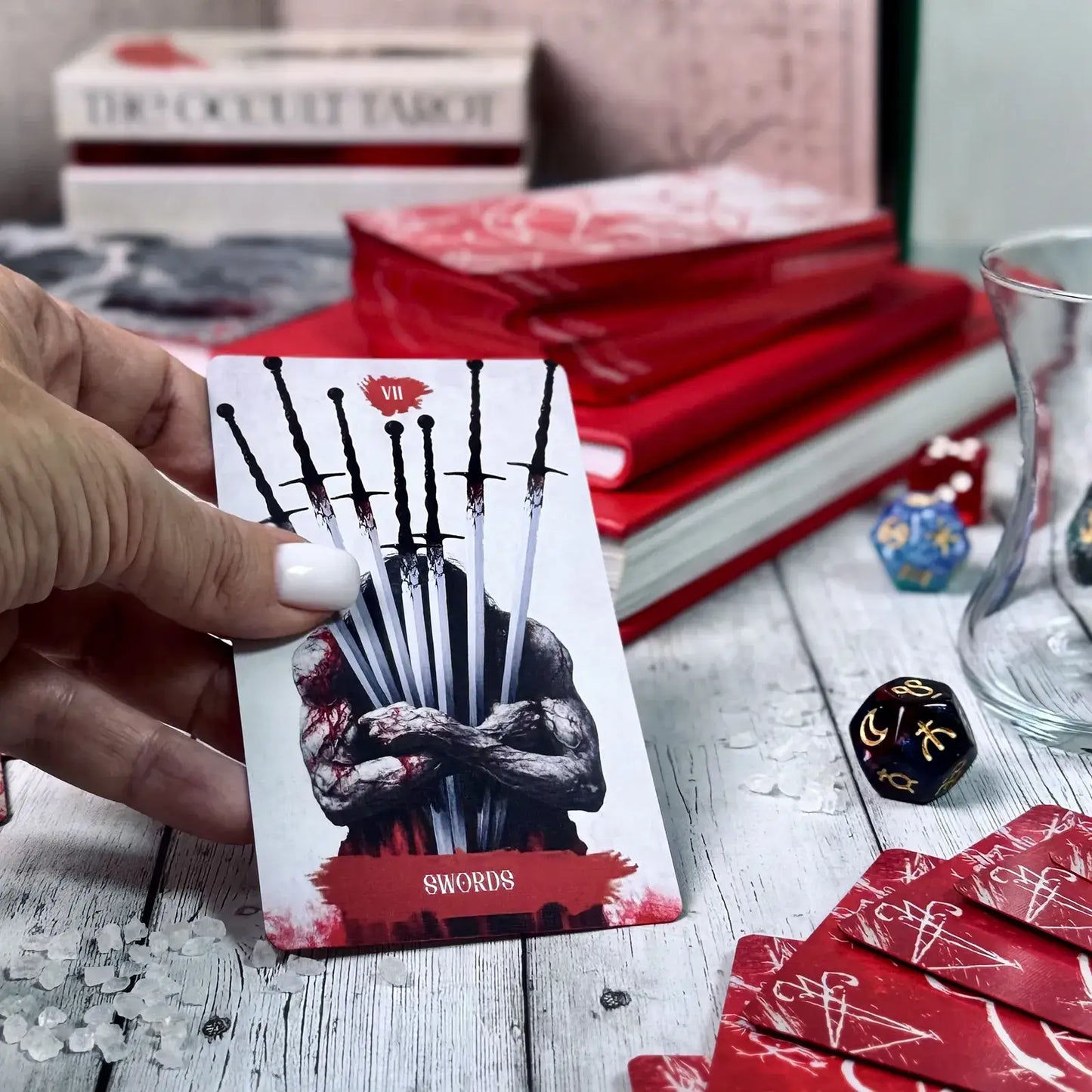 Card with a sword design held by a hand, surrounded by books and dice on a wooden surface.
