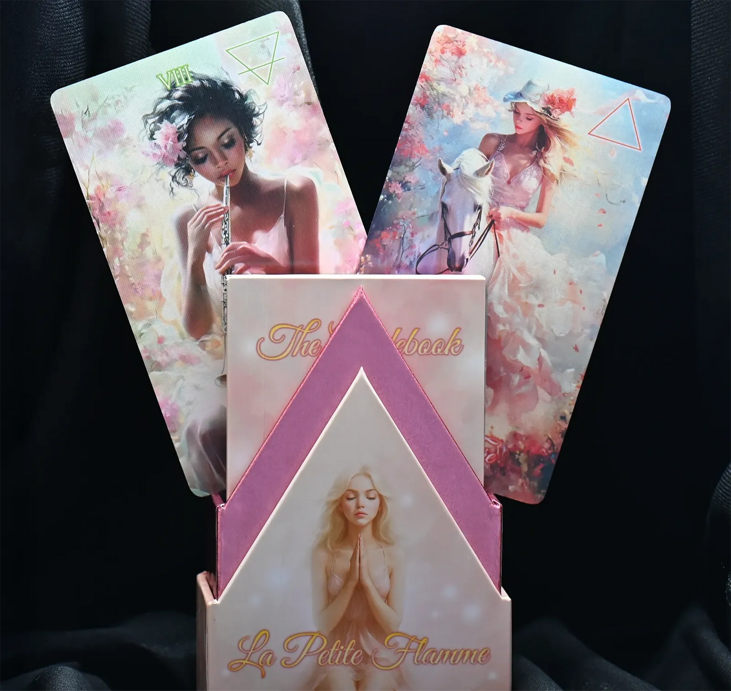 Three tarot cards with artistic designs and a pink box labeled 'La Petite Flamme' on a dark background.