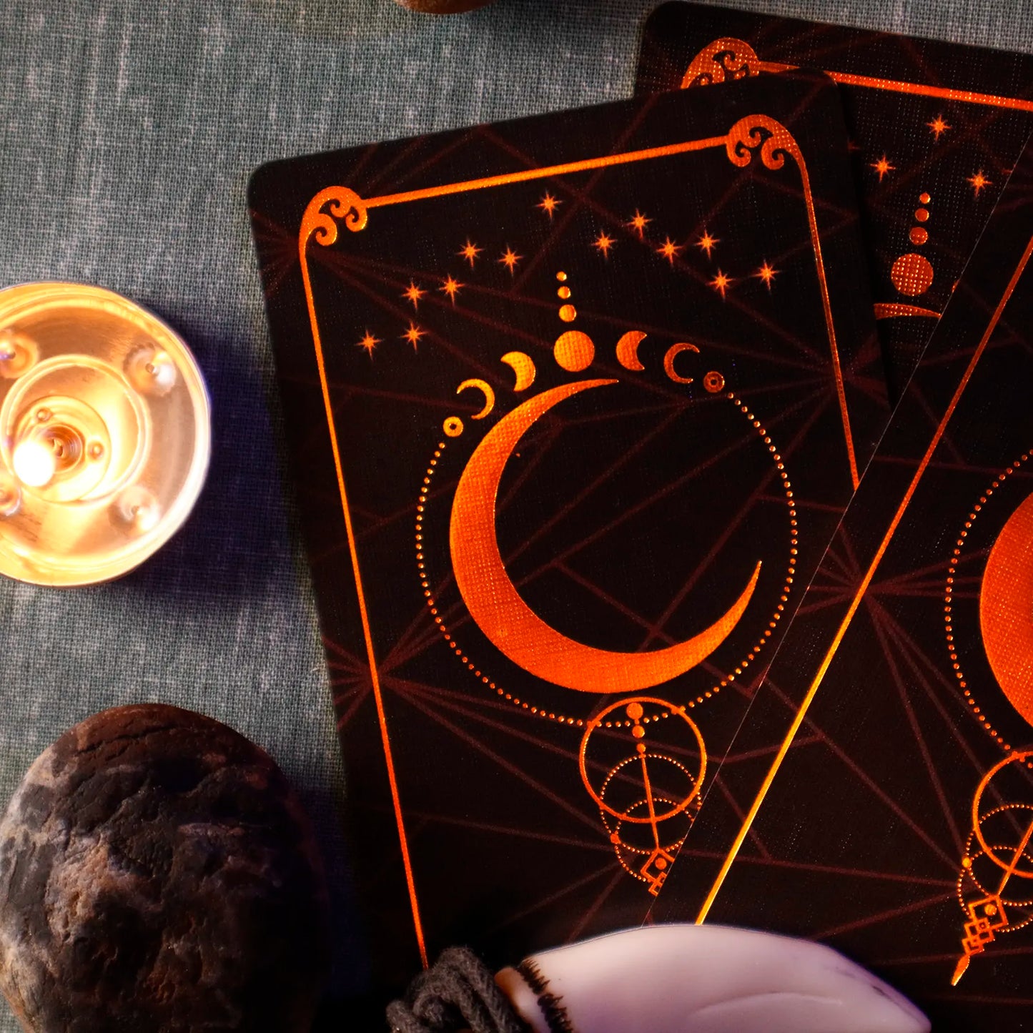 Black cards with orange crescent moon design on a textured surface with a candle and crystal ball.