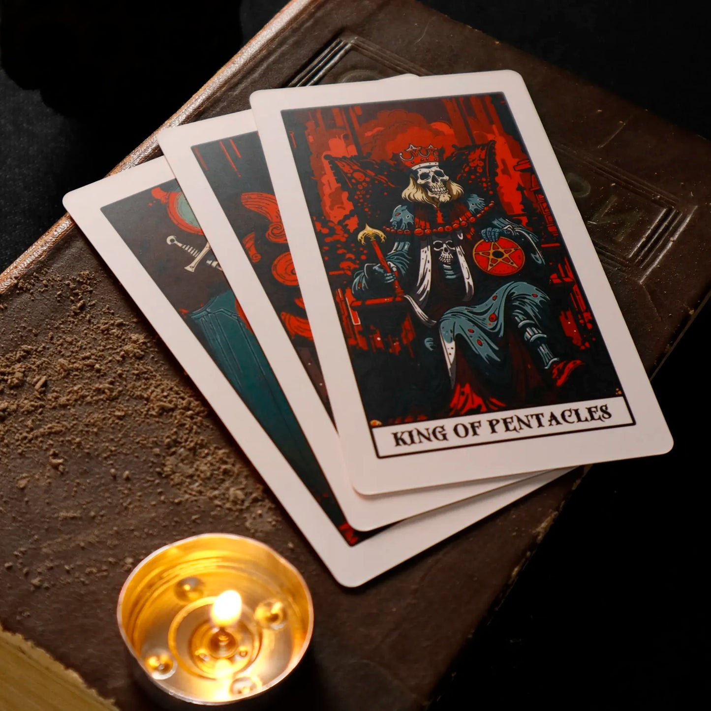 Three tarot cards on a dark surface with a lit candle.