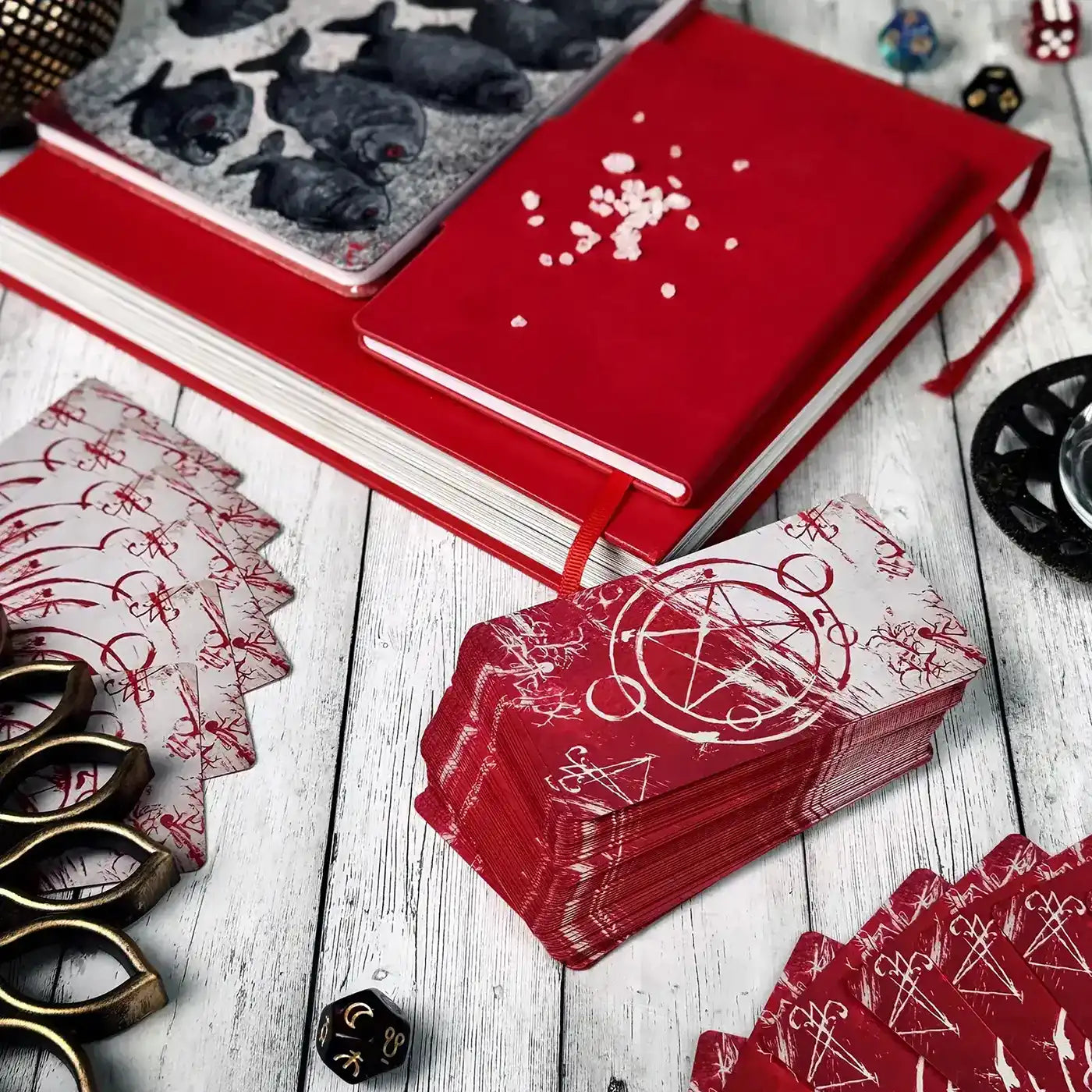 Red playing cards with black symbols on a wooden surface with dice and a notebook.