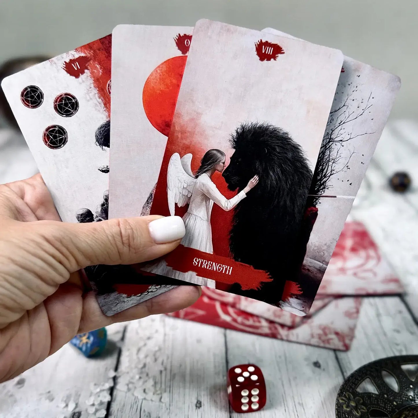 Hand holding tarot cards with 'Strength' card featuring a woman and horse, dice on wooden surface