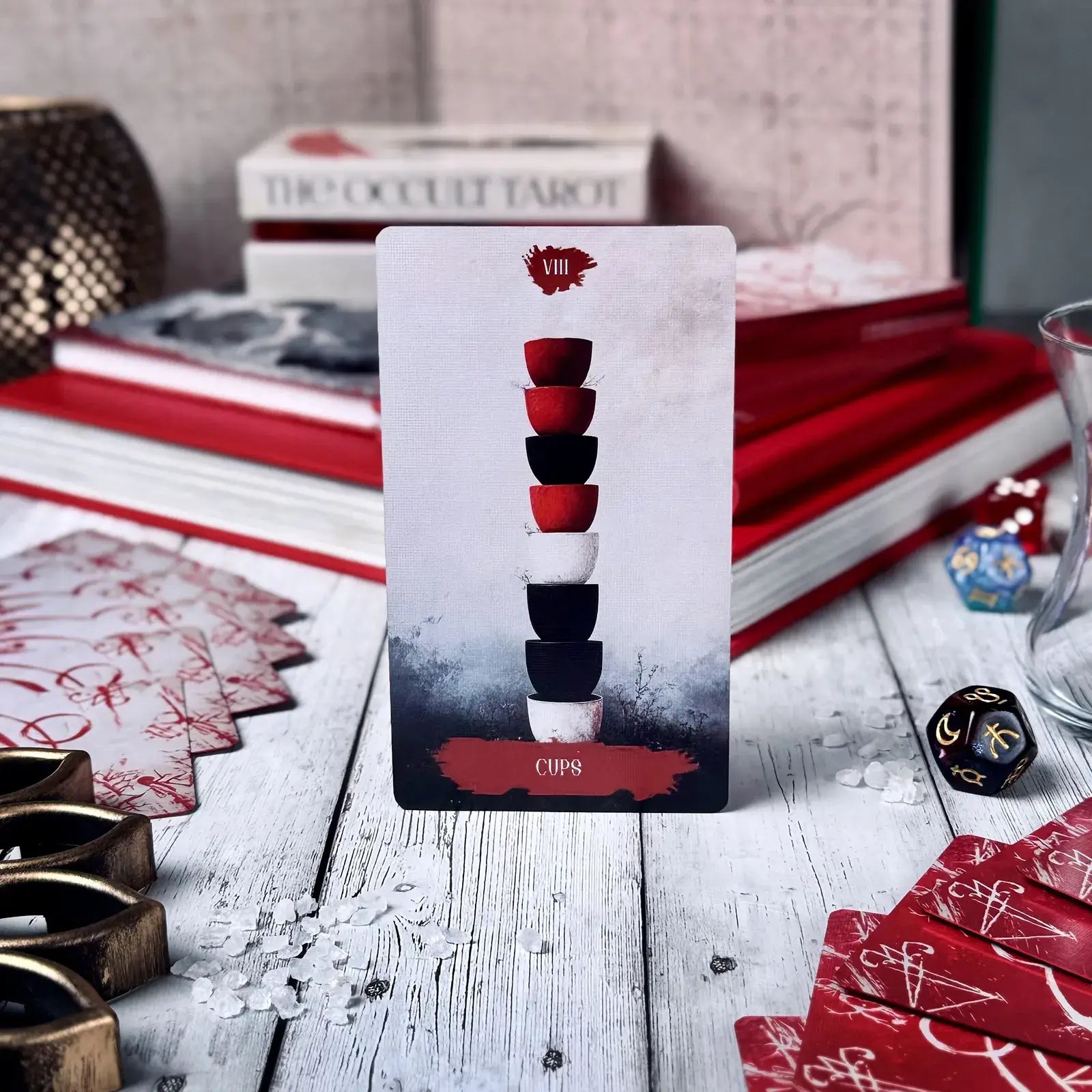 Tarot card with a stack of cups on a wooden surface with tarot books and cards.