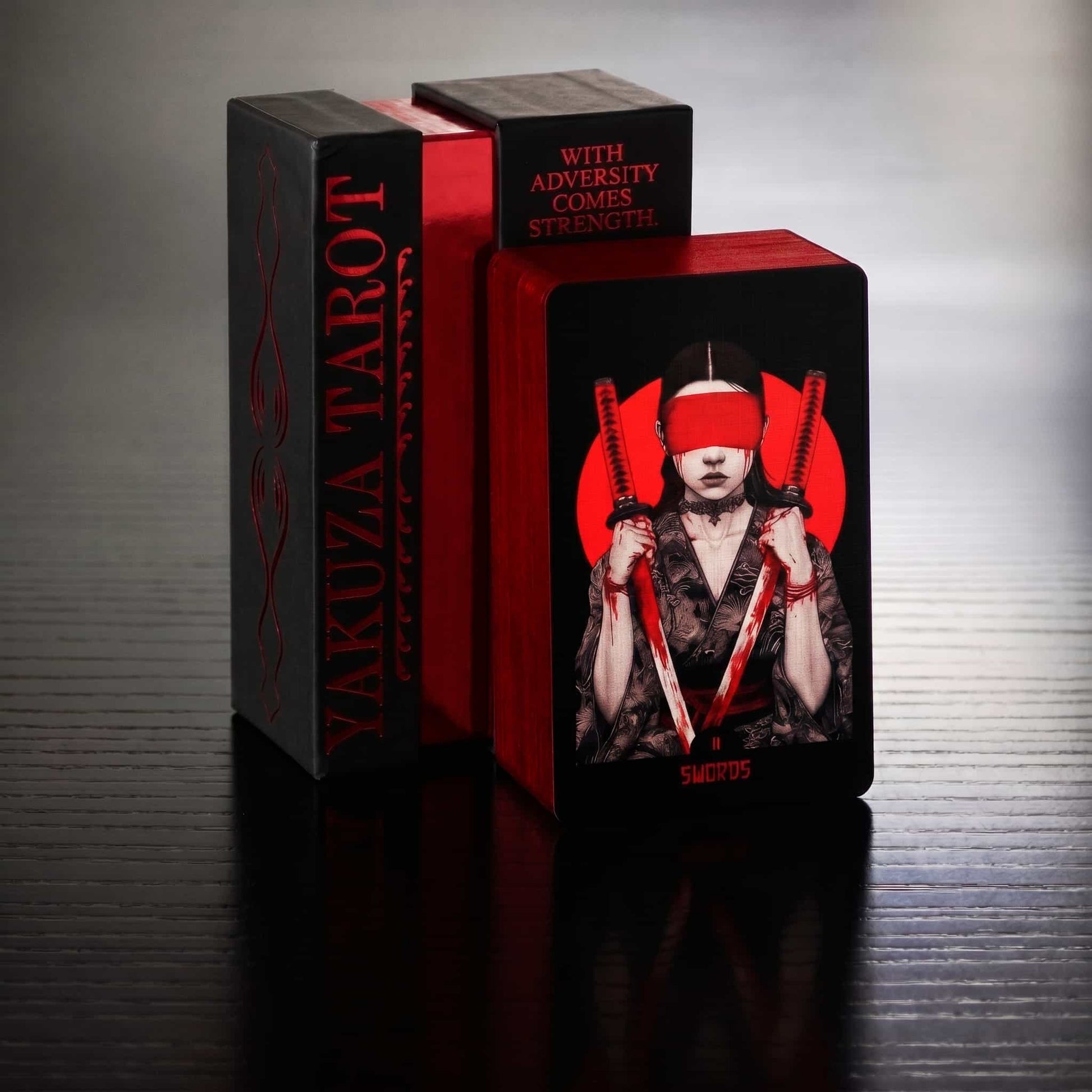 Yakuza Tarot card box and card with person holding two swords on a reflective surface. Card two of swords 