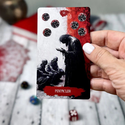 Arcana Obscura Six of Pentacles tarot card held in hand with red black design and symbolic figures