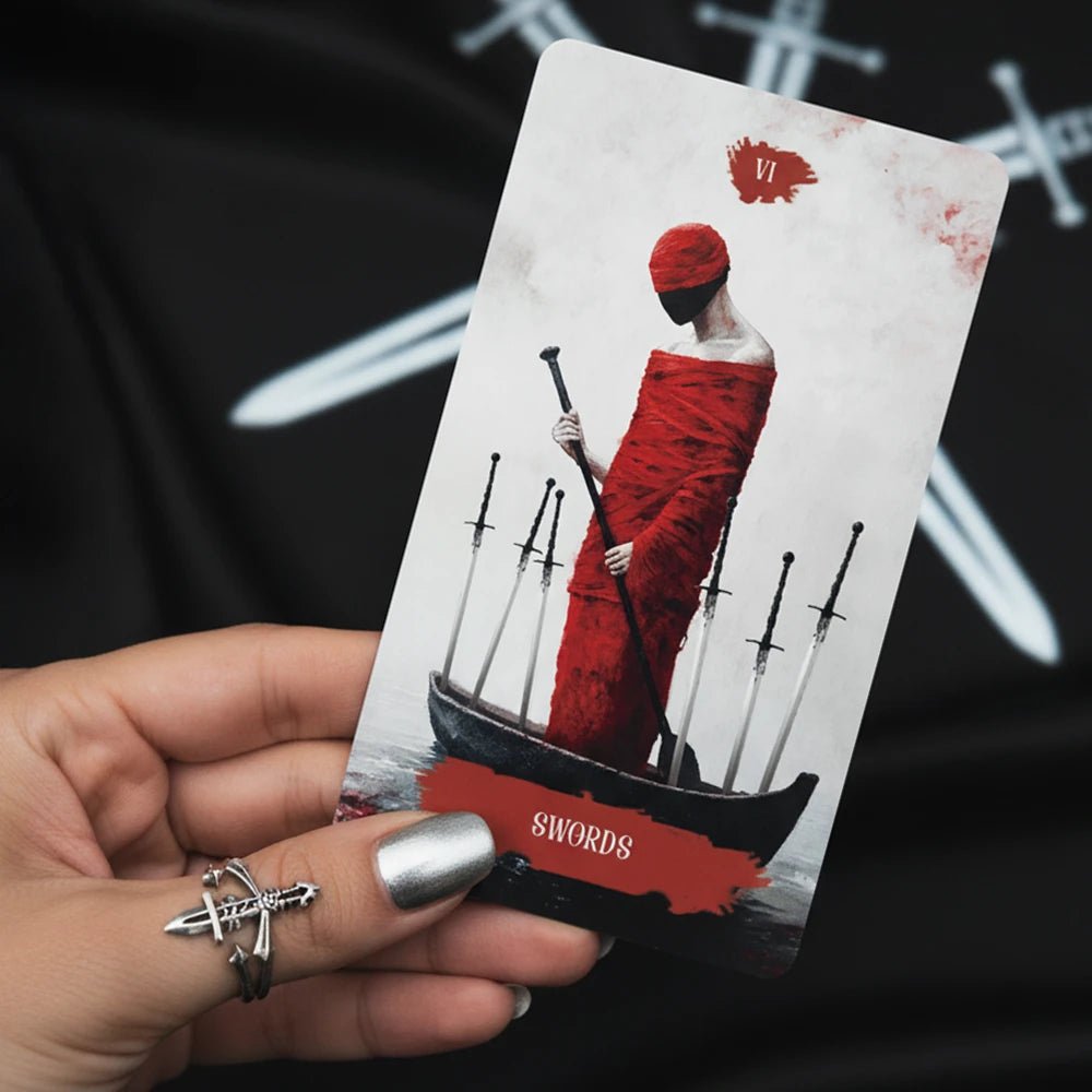 Arcana Obscura Six of Swords tarot card held in hand with red cloaked figure and swords composition