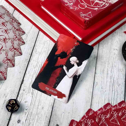 The Lovers tarot card from Arcana Obscura deck showing angel and shadow figure on wooden table with red books