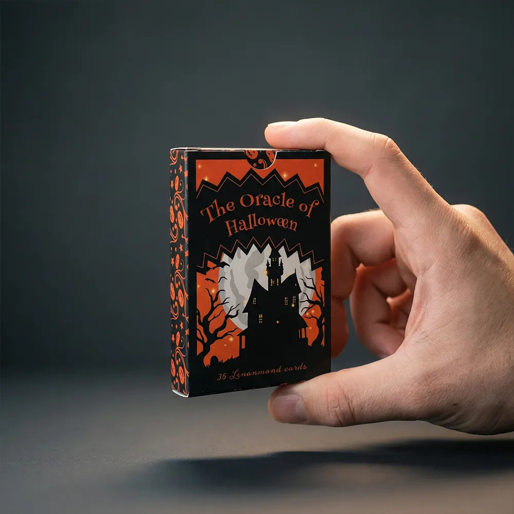 Hand holding The Oracle of Halloween Lenormand deck box against dark background