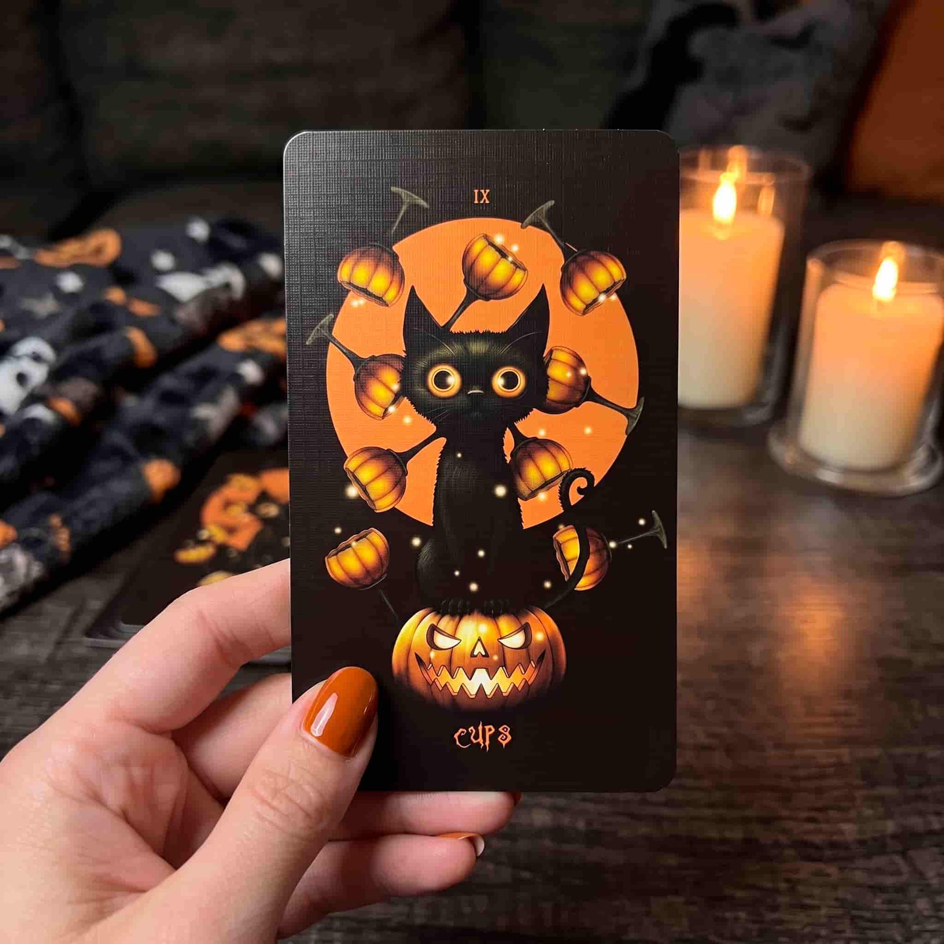 Halloween Tarot Nine of Cups card held in hand with candles, black orange artwork, pumpkin cat and seasonal Halloween atmosphere