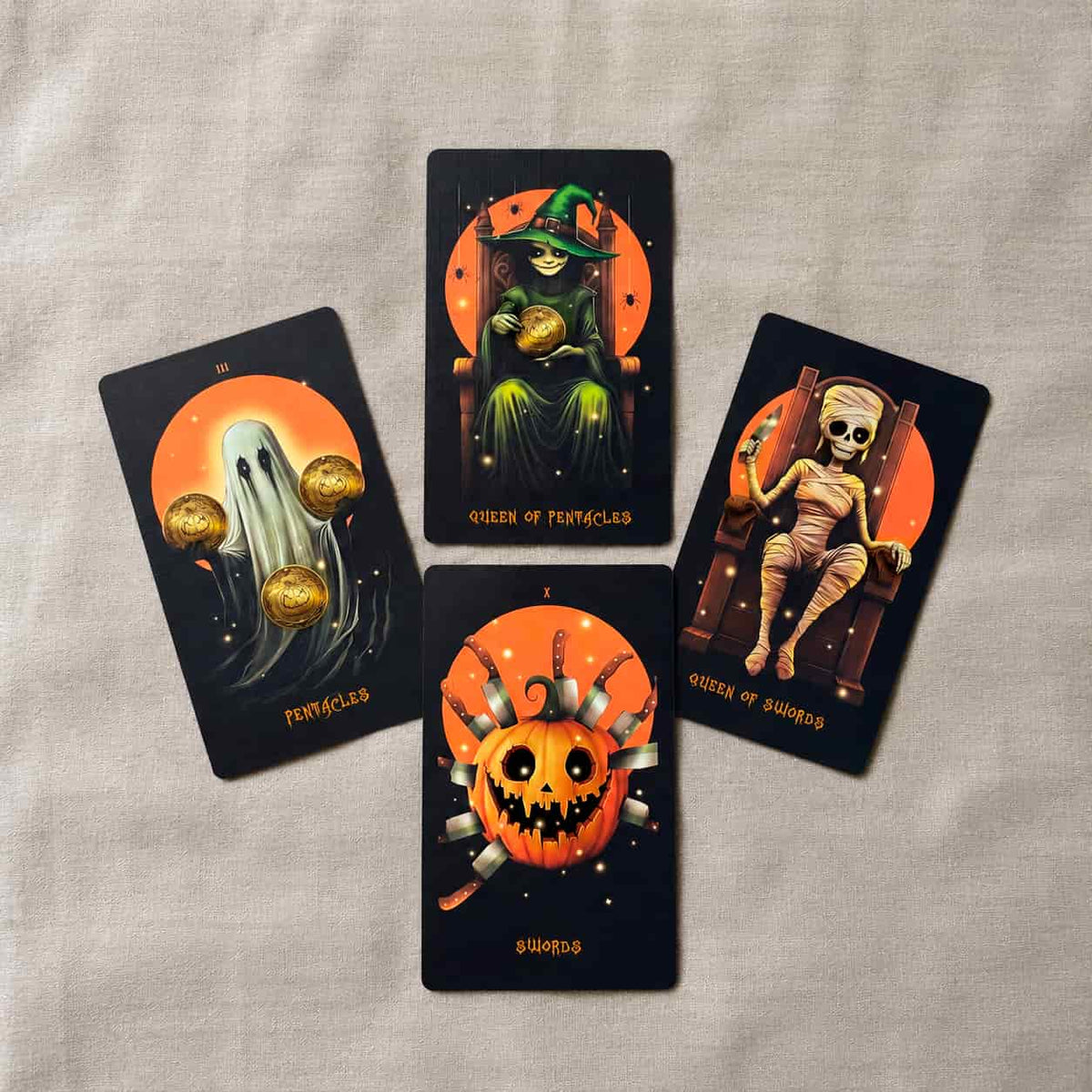 Halloween Tarot cards displayed on linen fabric, featuring Queen of Pentacles, Queen of Swords, Pentacles and Swords with black orange seasonal artwork
