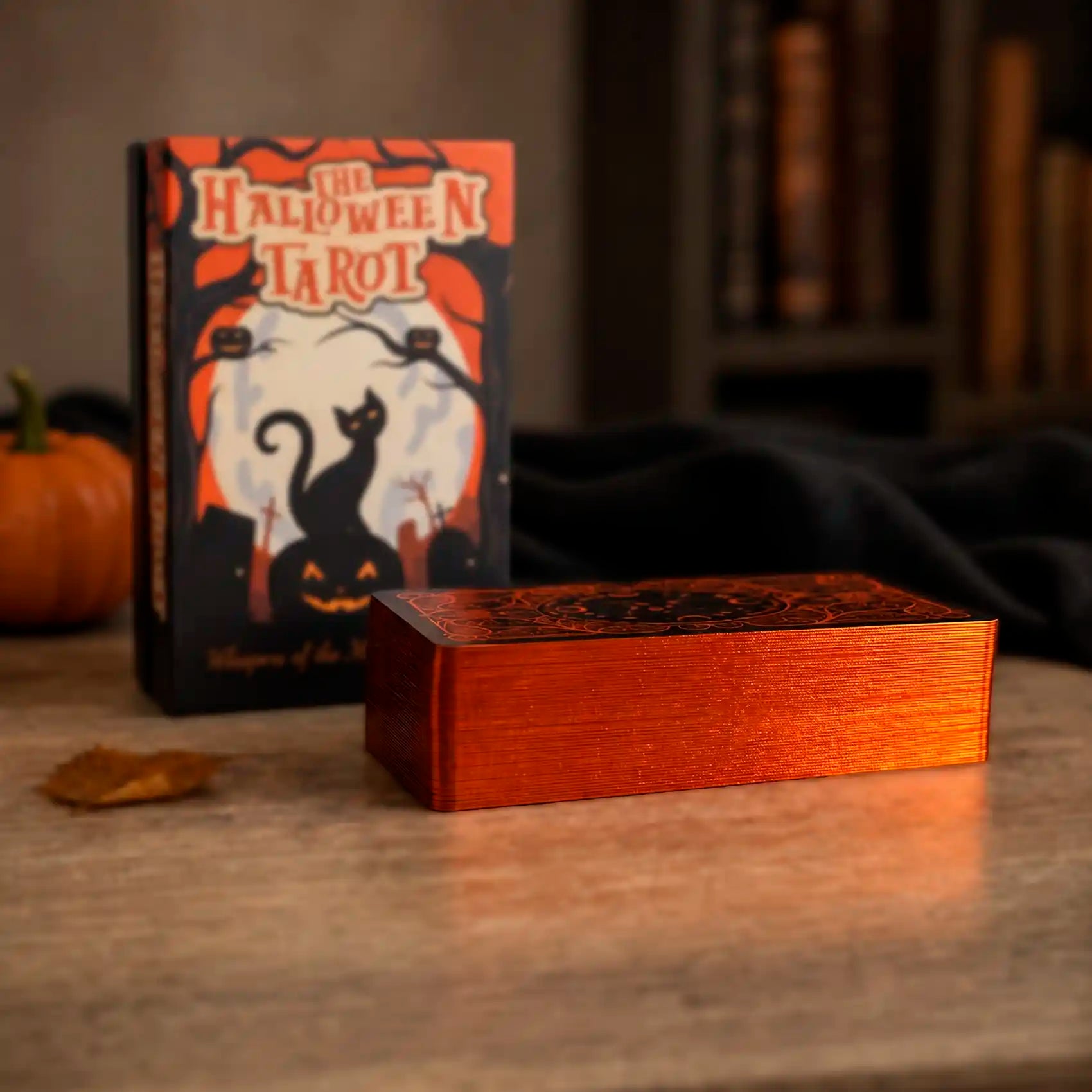 Halloween Tarot deck close-up showing pumpkin orange gilded edges with collector box in the background
