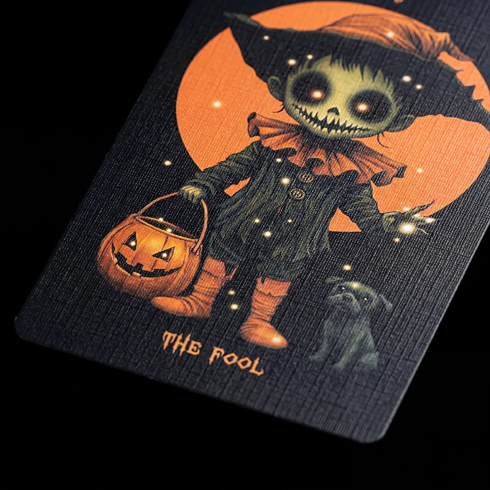 Close-up of Halloween Tarot The Fool card with pumpkin lantern and dark whimsical character