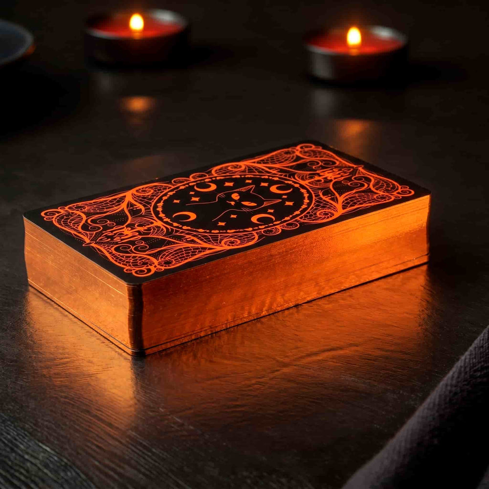 Halloween Tarot deck with pumpkin-orange gilded edges and black cat card back by candlelight