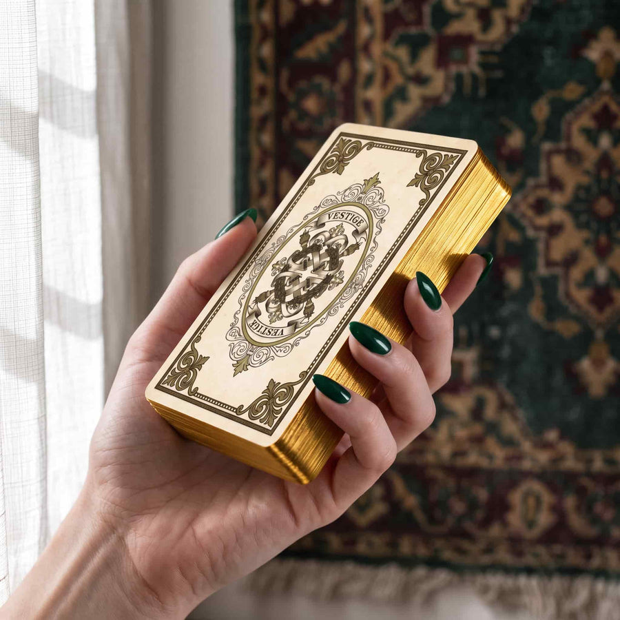 Hand holding Vestige Tarot deck, cream ornate card back and gold gilded edges