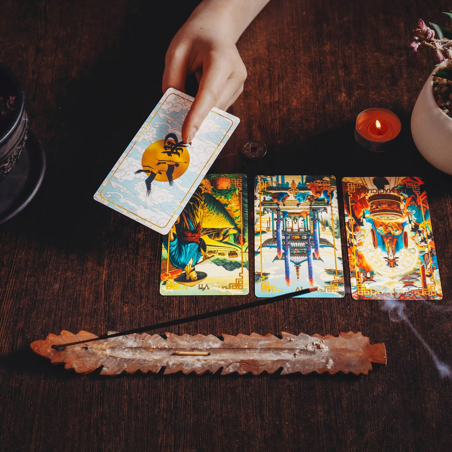 Hand laying out a Journey to the West Tarot spread with incense, card back with cranes over a golden sun