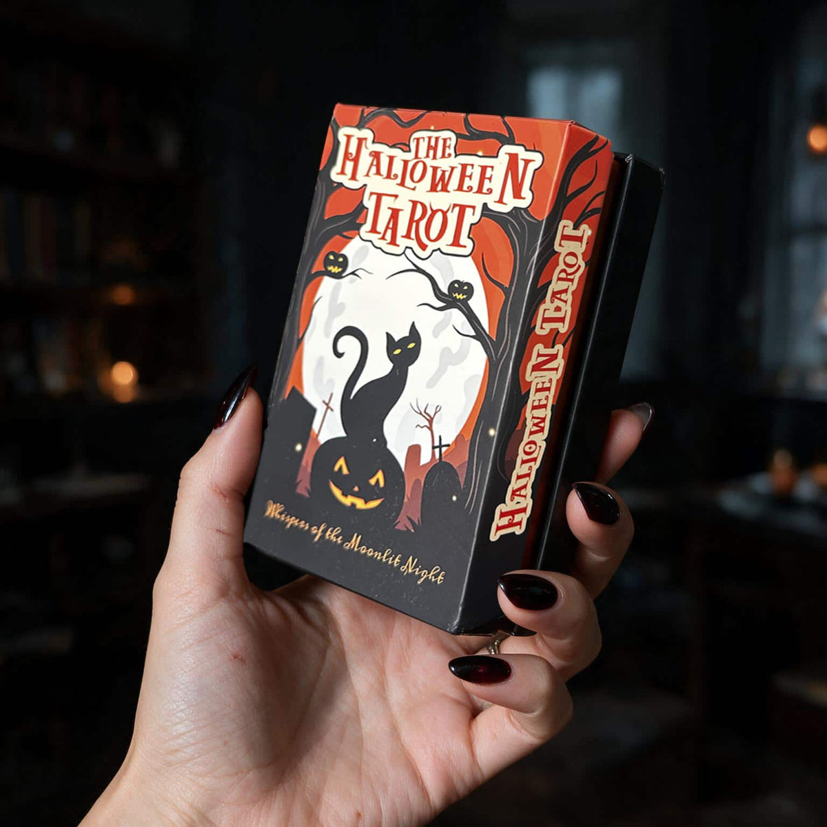 Hand holding The Halloween Tarot box with black cat on jack-o'-lantern under full moon