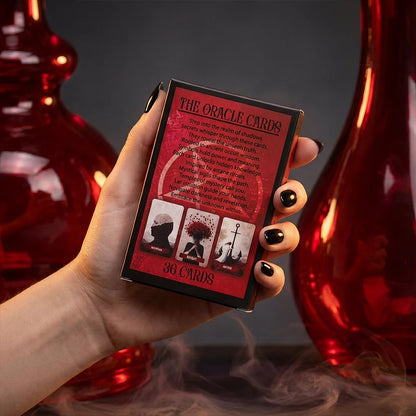 Back of oracle cards box with red occult design and description text held in hand with dark aesthetic background and smoke