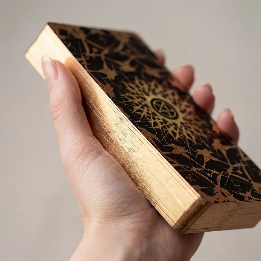 Hand holding Persona Obscura Tarot deck showing gold gilded edges, ornate black-and-gold back design