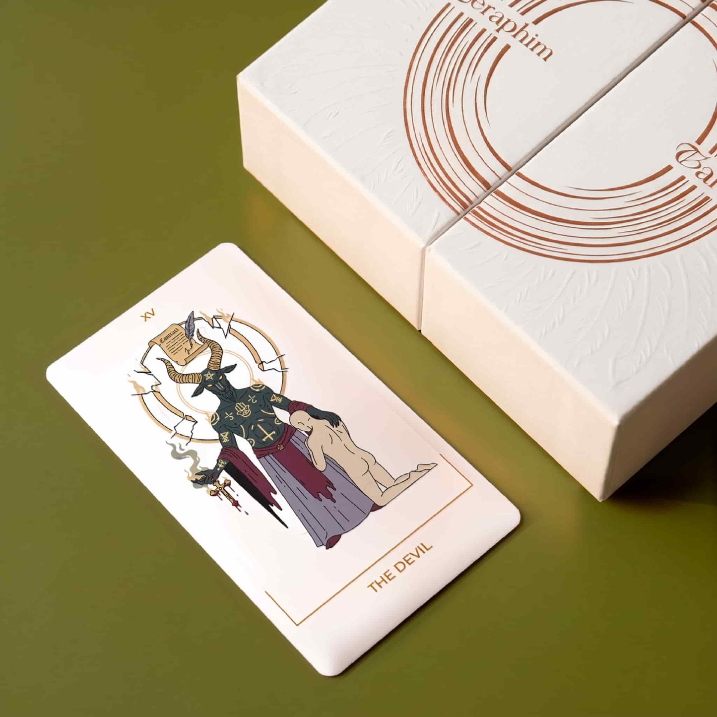 Close-up of The Devil card beside the embossed Seraphim Tarot collector box with gold foil detailing.