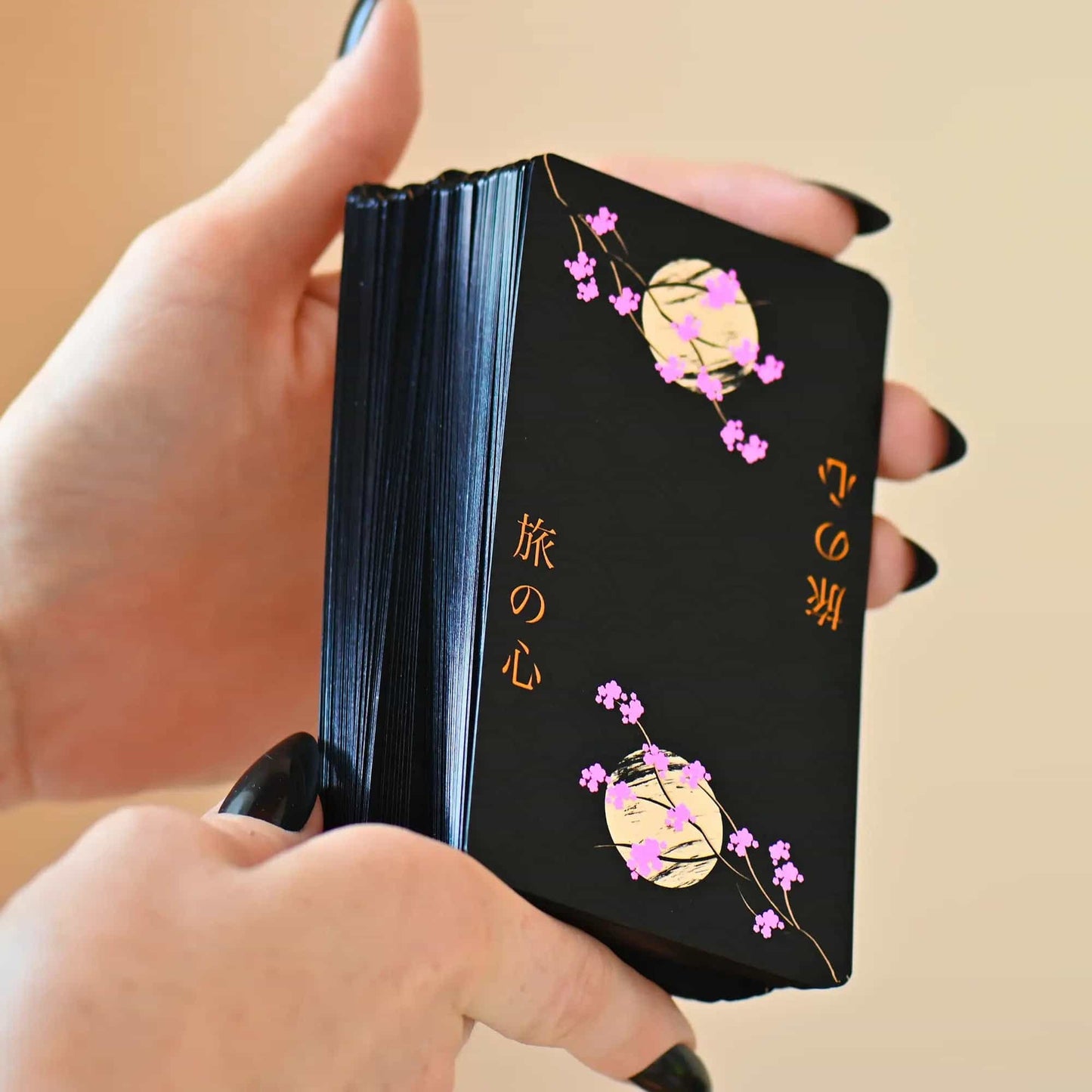 Black cardholder with floral designs and text held by a hand against a beige background