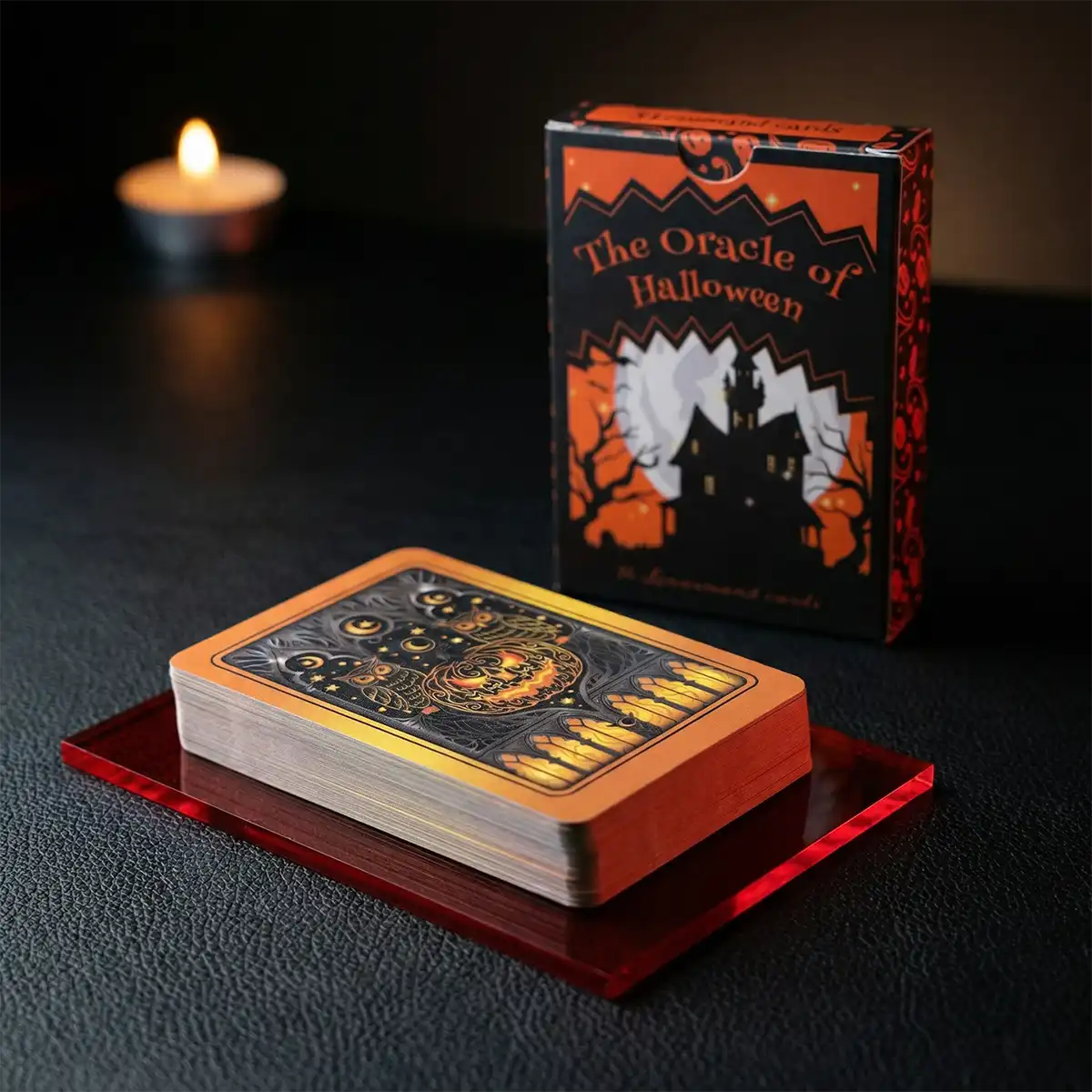 The Oracle of Halloween deck and collector box on a dark surface with a candle in the background