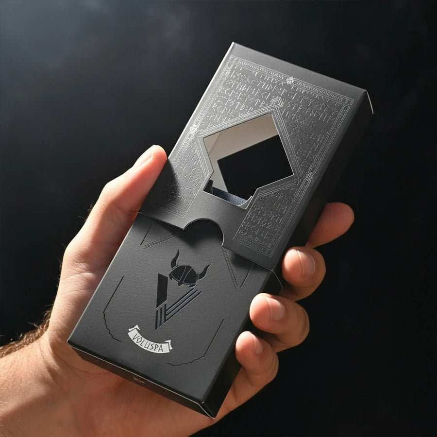 Hand holding Völuspá playing cards box with die-cut window, silver runes and Viking helmet logo